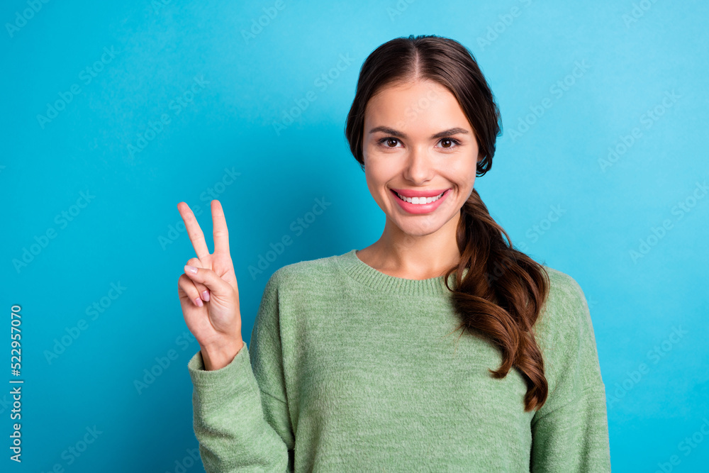 Photo of adorable positive lady toothy smile hand fingers demonstrate v-sign isolated on blue color background Photo of adorable positive lady toothy smile hand fingers demonstrate v-sign isolated on blue color background