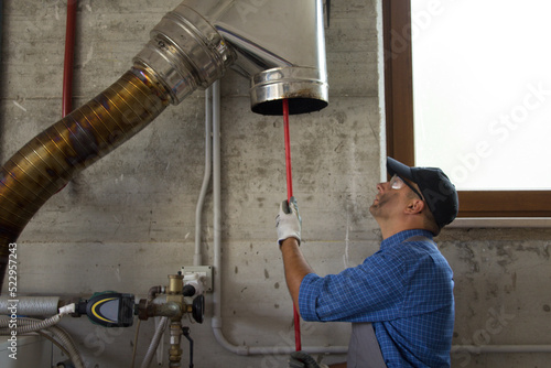 Fotografering Picture of a handyman cleaning the stainless steel pipe of a boiler flue with a brush