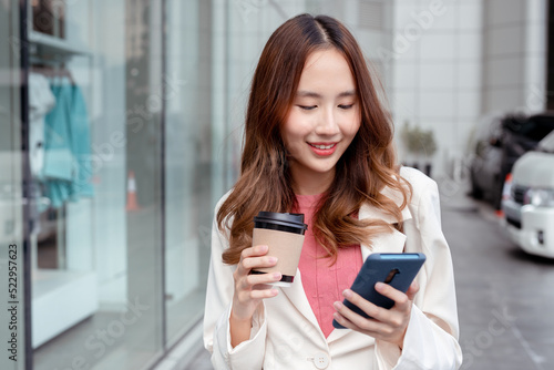 Beautiful asian female businesswoman use smartphone hold paper cup of hot drink, Walk enjoy smiling while doing commuting in the modern city near office building outside Free Download Beautiful asian female businesswoman use smartphone hold paper cup of hot drink, Walk enjoy smiling while doing commuting in the modern city near office building outside - GFXLoad