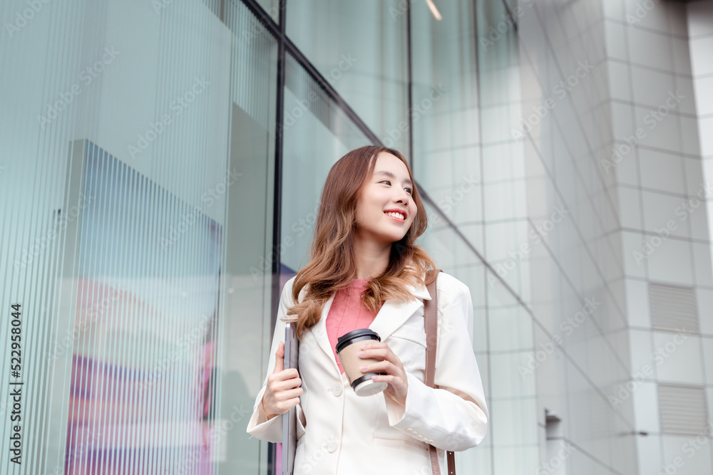 Beautiful asian female businesswoman hold laptop computer and paper cup of hot drink, Walk enjoy smiling while doing commuting in the modern city near office building outside Beautiful asian female businesswoman hold laptop computer and paper cup of hot drink, Walk enjoy smiling while doing commuting in the modern city near office building outside