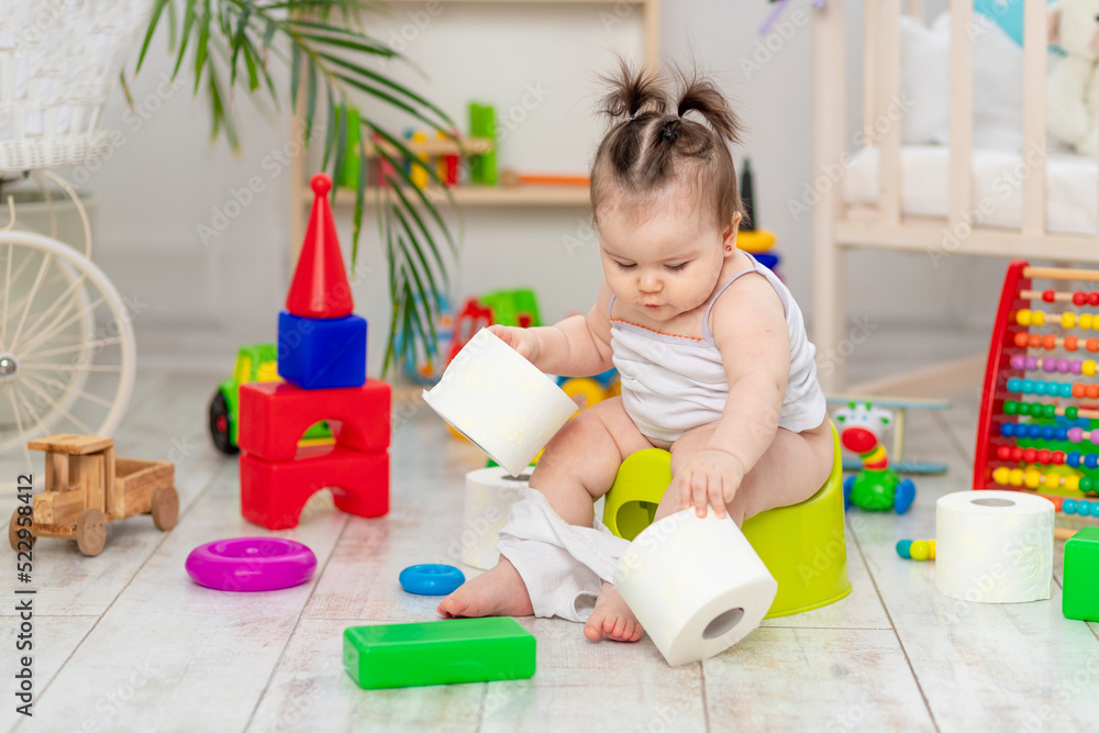 baby on a potty pees and plays with toilet paper in the children's room at home baby on a potty pees and plays with toilet paper in the children's room at home