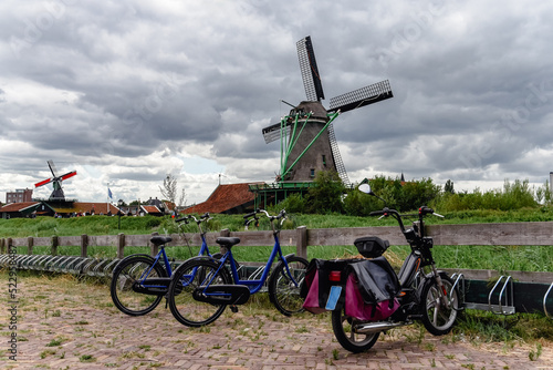 Tres bicicletas aparcadas en el pueblo de Zaanse Schans. Al fondo, varios molinos de viento tradicionales de los Países Bajos. photo