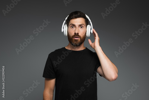 surprised man touching wireless headphones and listening music isolated on grey.