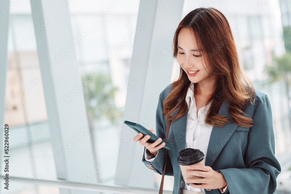 Beautiful asian female businesswoman use smartphone hold paper cup of hot drink, Walk enjoy smiling while doing commuting in the modern city at office Beautiful asian female businesswoman use smartphone hold paper cup of hot drink, Walk enjoy smiling while doing commuting in the modern city at office