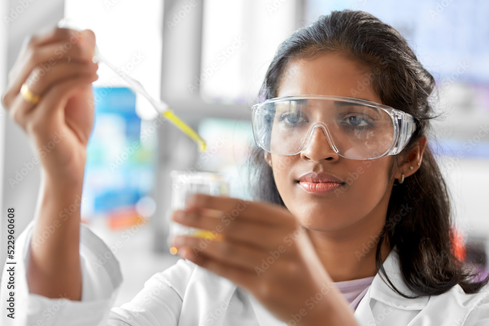 science research, work and people concept - female scientist in goggles with dropper and chemical or test sample in beaker working in laboratory science research, work and people concept - female scientist in goggles with dropper and chemical or test sample in beaker working in laboratory
