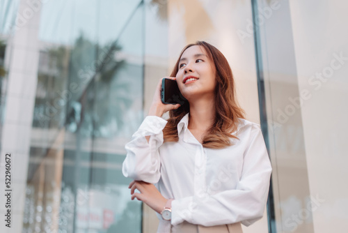 Beautiful asian female businesswoman use smartphone, Walk enjoy smiling while doing commuting in the modern city near office building outside.
