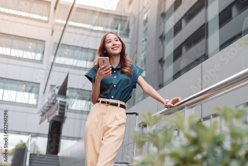 Beautiful asian female businesswoman use smartphone  Walk enjoy smiling while doing commuting in the modern city near office building outside