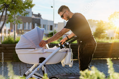 Portrait of a young father while walking with a child in a stroller. A man walks with a baby in a stroller around the city.