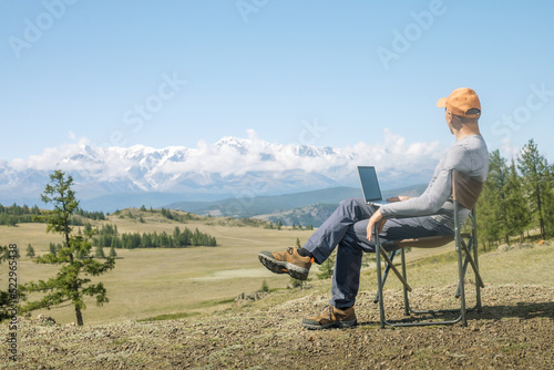 Mature man traveler uses laptop computer on mountain top,  enjoying nature landscape view outdoors. work remote concept. © Sergey
