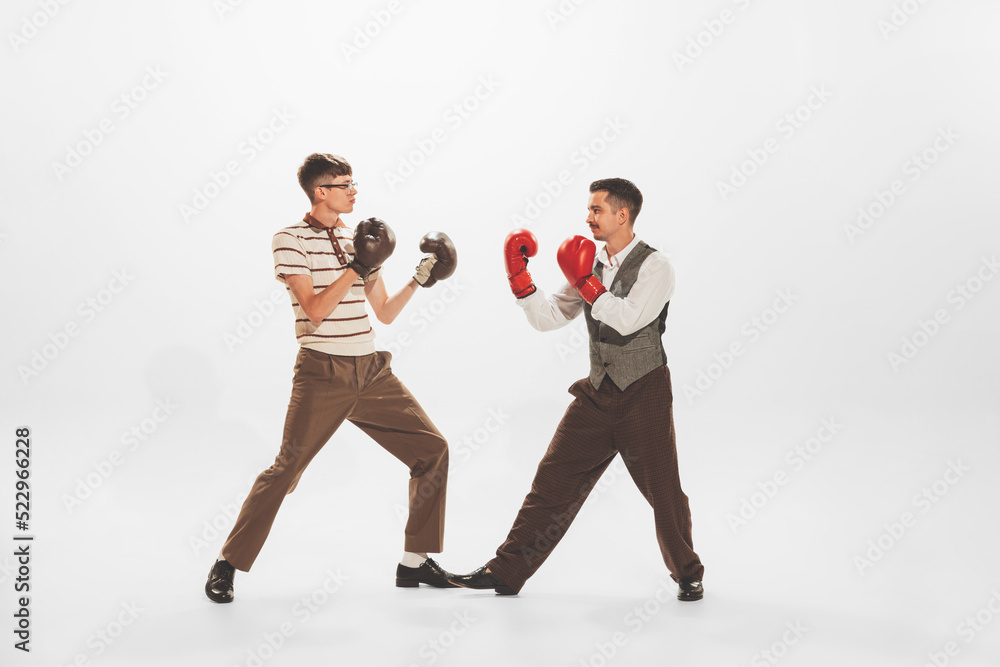 Portrait of two men in retro clothes, suits fighting for fun, boxing isolated over white studio background