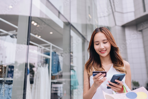 Shopper customer asian woman using credit card and smartphone for payment to owner at shopping mall outside, cashless technology payment shopping in the city