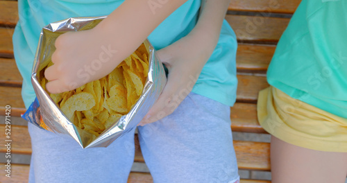 Two pretty kids eat delicious chips outdoor.