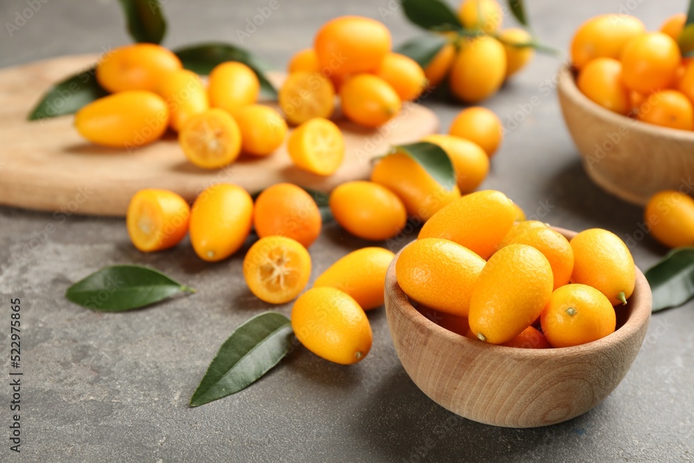 Fresh ripe kumquats in bowl on grey table, space for text