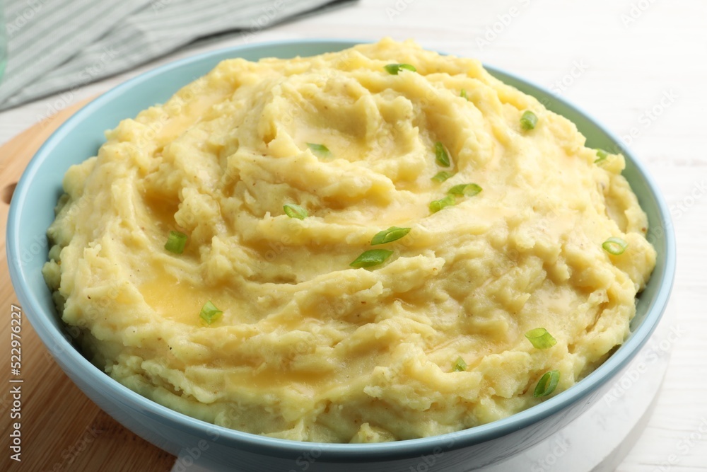 Bowl of tasty mashed potatoes with onion served on white wooden table, closeup