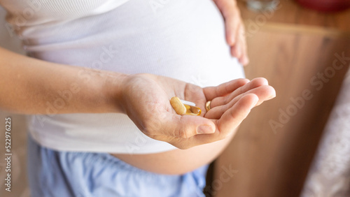 Pregnant woman pills vitamin. Happy smiling woman taking pill with supplement vitamin Omega 3. Vitamin D, E, A Fish Oil Capsules.