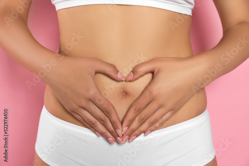 Woman in underwear making heart with hands on her belly against pink background  closeup. Healthy stomach