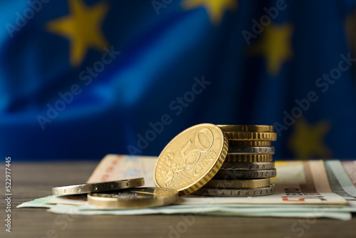 Coins and banknotes on wooden table against European Union flag, space for text photo