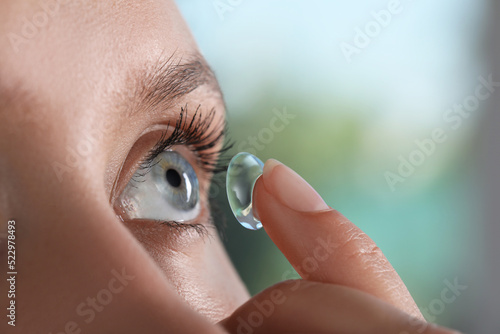 Cuadro en lienzo Young woman putting contact lens in her eye on blurred background, closeup