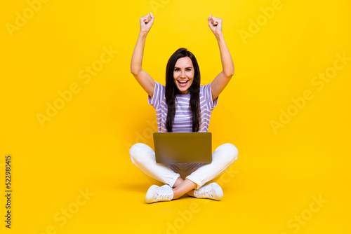 Photo of positive satisfied lady sit empty space crossed legs arm raised rejoice pass distance test isolated on yellow color background © deagreez