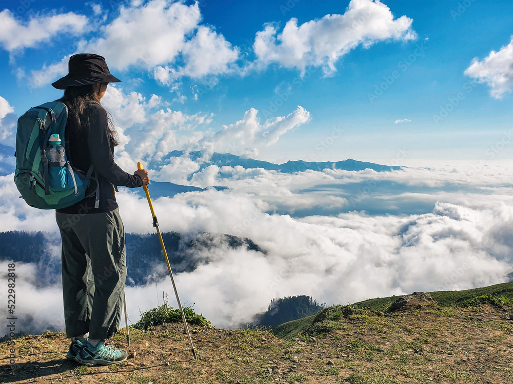 Young active woman with backpack hiking at cloudscape and mountains background