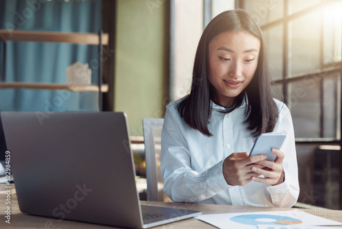 Attractive asian businesswoman working on laptop and using phone at modern office