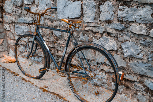 An old rusty two-wheeled bicycle stands against the background of a stone wall, ancient means of transportation.