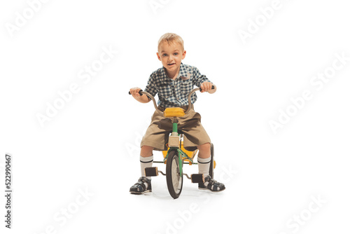Cute happy kid, little boy riding tricycle isolated on white studio background. Retro vintage style concept. Friendship, hobbies, art, eras comparison