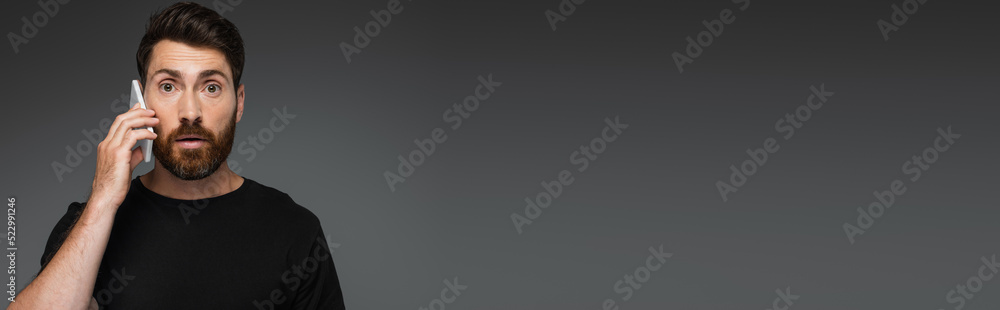 shocked man in black t-shirt talking on smartphone isolated on grey, banner. shocked man in black t-shirt talking on smartphone isolated on grey, banner.