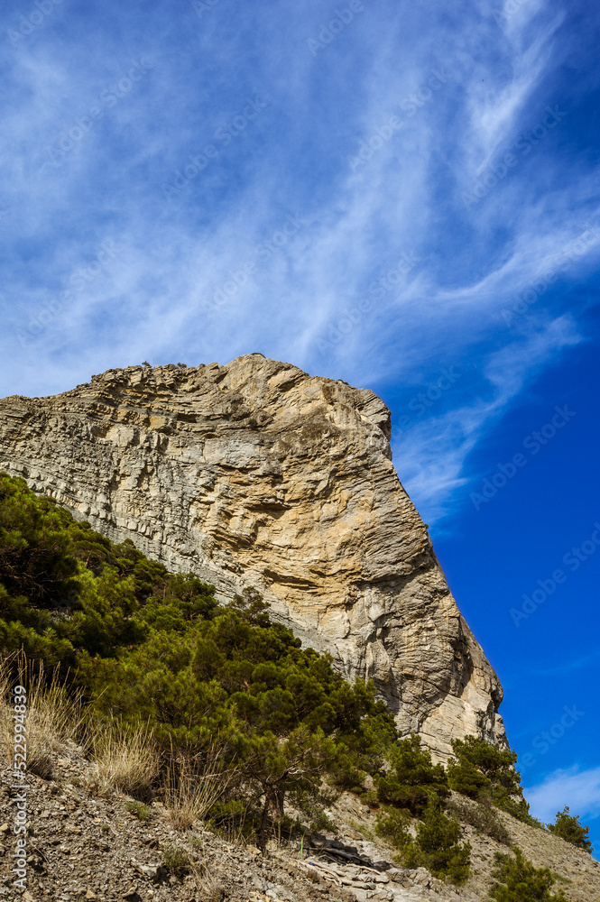 Bottom view of huge rock. Clouds in blue sea. Mountain.