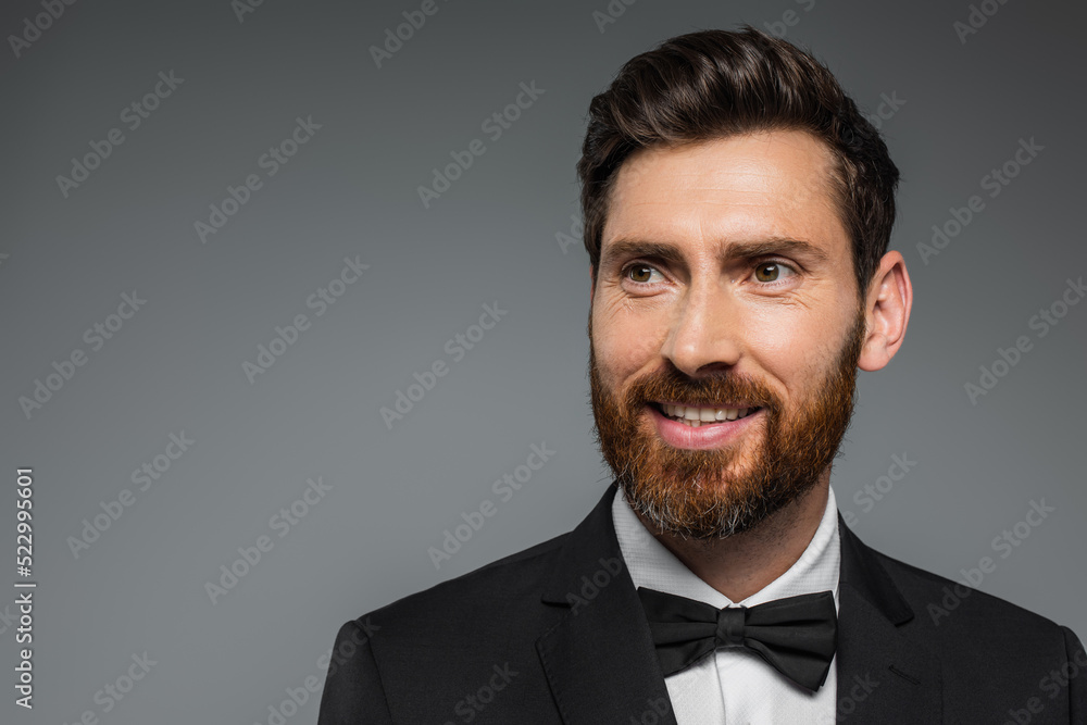 cheerful and bearded man in black tuxedo with bow tie isolated on grey. cheerful and bearded man in black tuxedo with bow tie isolated on grey.