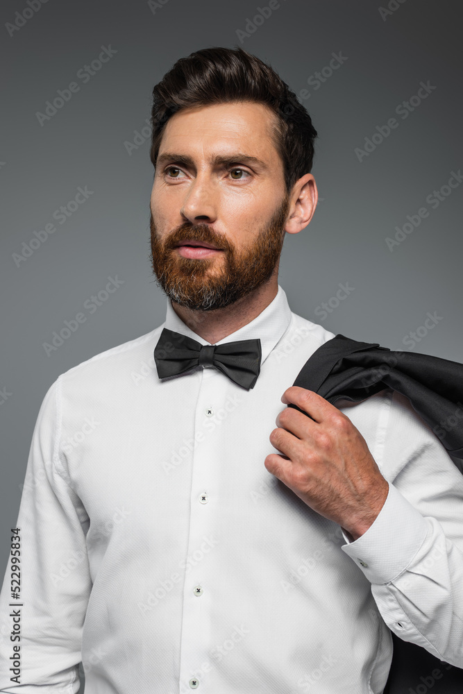 portrait of bearded man in suit with bow tie holding blazer isolated on grey. portrait of bearded man in suit with bow tie holding blazer isolated on grey.