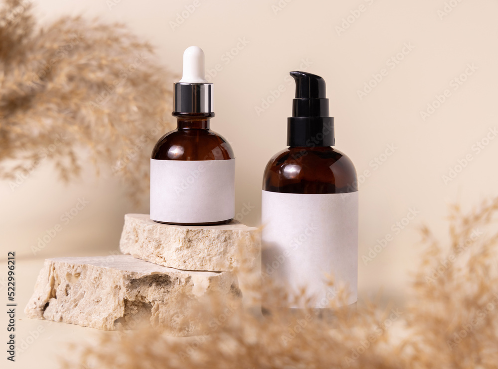 Cosmetic bottles on beige stones near dry pampas grass on light beige close up. Labels Mockup