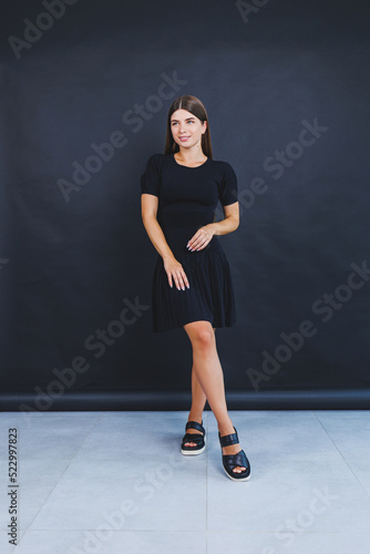 A pretty young woman in a black short dress and light leather sandals. Women's summer fashion