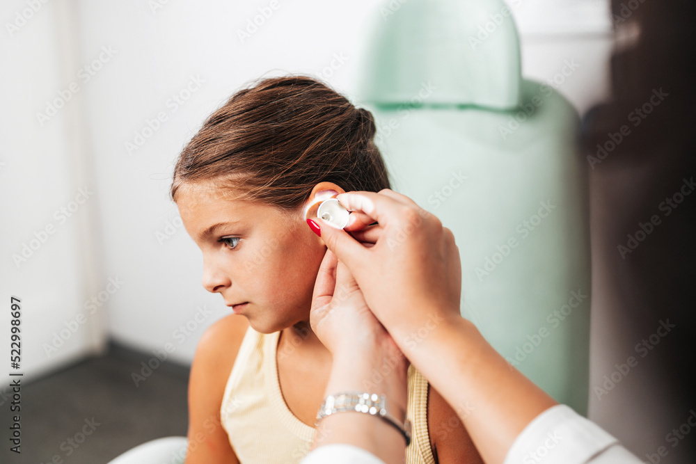 Female audiologist examining girl ear using otoscope in doctors office