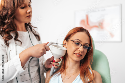Otolaryngologist doing ear irrigation and earwax removal to a young adult woman with modern medical equipment. Healthcare and medicine concept. photo