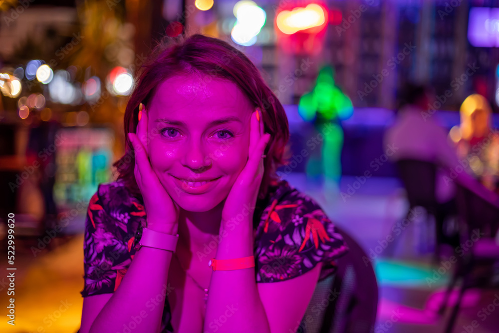 A beautiful girl sits at the bar and smiles. Portrait of a beautiful girl. Neon lights. Girl at night in a bar. Beautiful light.