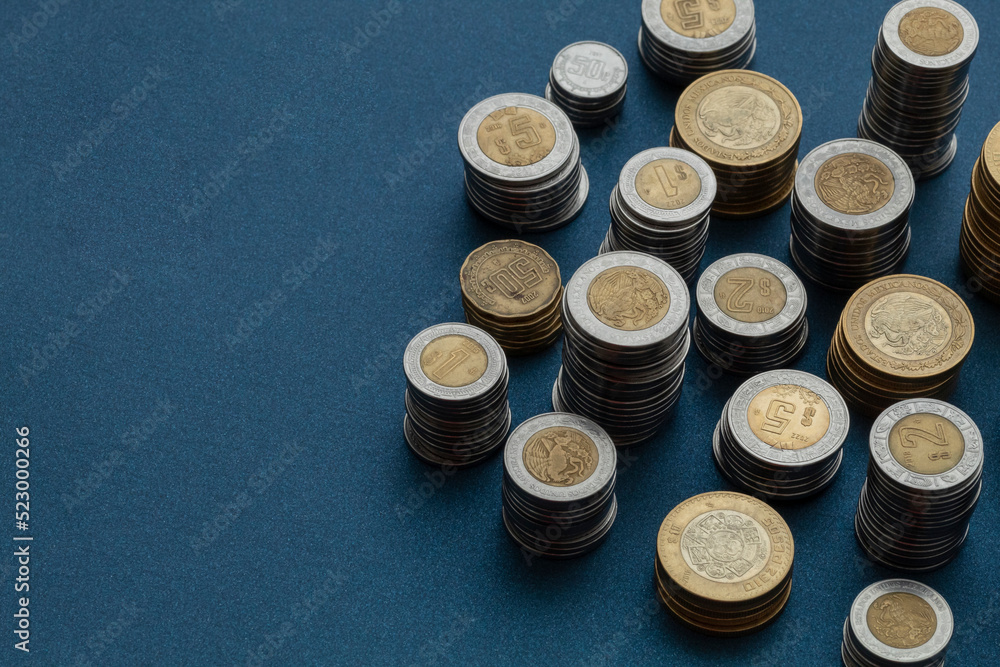 Piles of Mexican pesos coins arranged in the corner of the image with copy space and a blue background Piles of Mexican pesos coins arranged in the corner of the image with copy space and a blue background