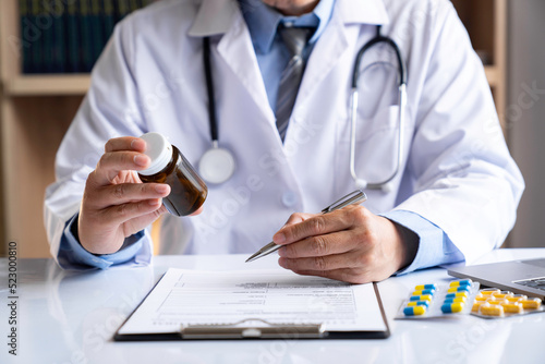 Fotografie male medicine doctor hand holds the bottle of pills and writes a prescription to the patient at the worktable