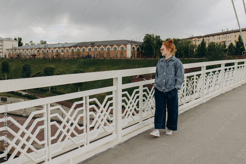 Red-haired girl walks along the city bridge