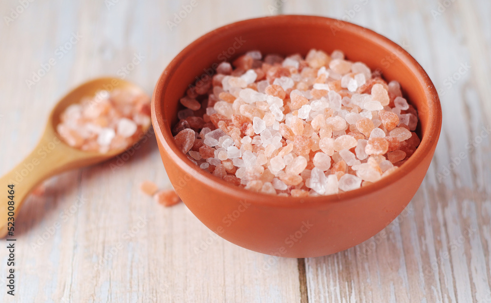 A wooden spoon and a ceramic bowl with pink Himalayan salt A wooden spoon and a ceramic bowl with pink Himalayan salt
