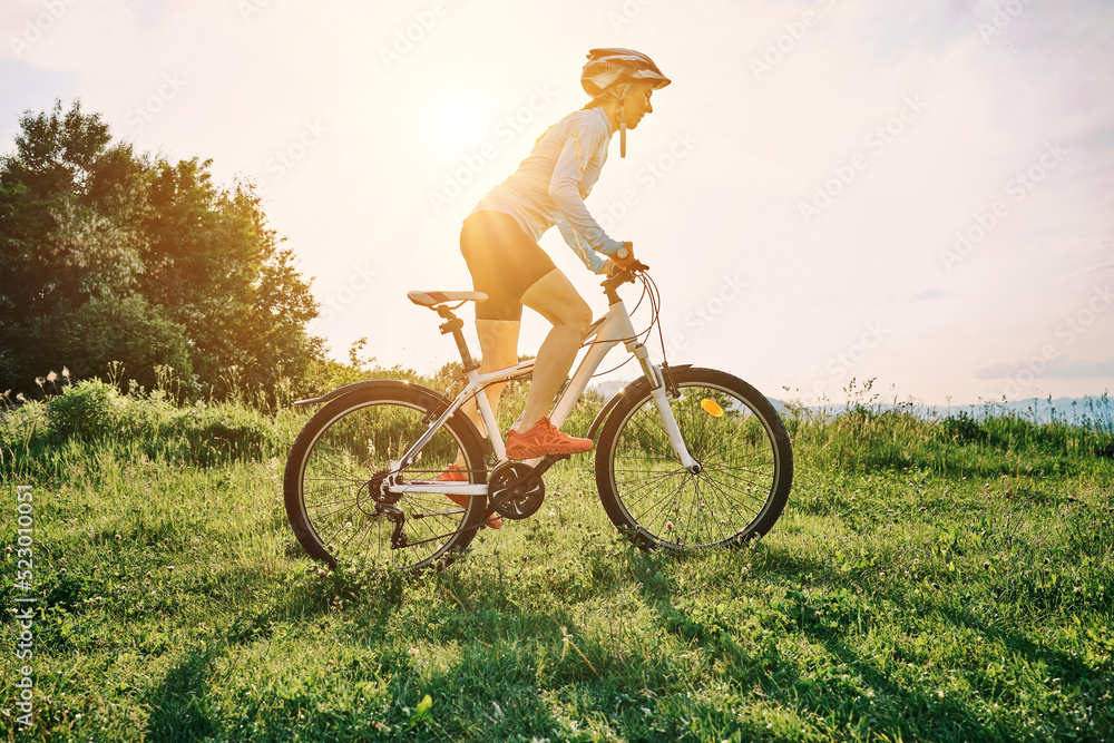 Obraz premium Cyclist Woman riding bike in helmets go in sports outdoors on sunny day a mountain in the forest. Silhouette female at sunset. Fresh air. Health care, authenticity, sense of balance and calmness. 