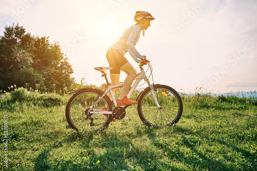Fototapeta Naklejka Na Ścianę i Meble -  Cyclist Woman riding bike in helmets go in sports outdoors on sunny day a mountain in the forest. Silhouette female at sunset. Fresh air. Health care, authenticity, sense of balance and calmness.	
