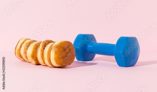 Donuts and blue dumbell on pastel background.  Calories need workout concept.