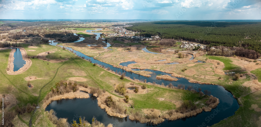 Spring aerial panorama view on green river delta valley from drone. Zmiyevsky region on Siverskyi Donets River in Ukraine. River curve under cloudy sky