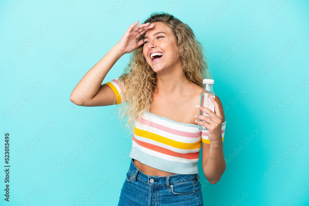 Young blonde woman with a bottle of water isolated on blue background smiling a lot Young blonde woman with a bottle of water isolated on blue background smiling a lot