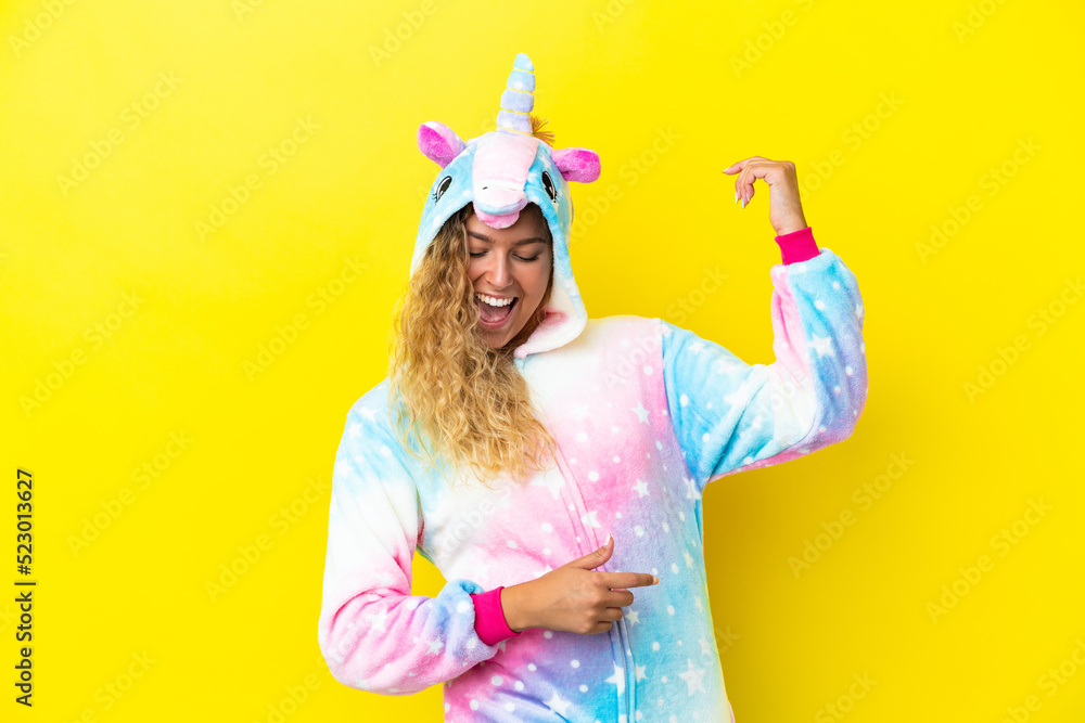 Girl with curly hair wearing a unicorn pajama isolated on yellow background making guitar gesture Girl with curly hair wearing a unicorn pajama isolated on yellow background making guitar gesture