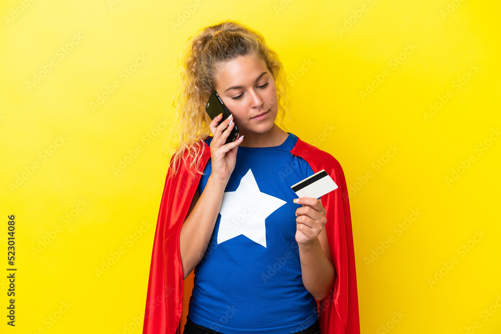 Super Hero woman isolated on yellow background buying with the mobile with a credit card Super Hero woman isolated on yellow background buying with the mobile with a credit card