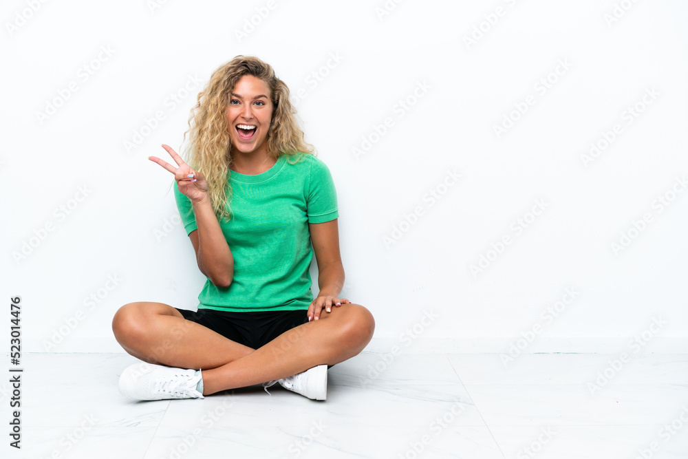 Girl with curly hair sitting on the floor smiling and showing victory sign Girl with curly hair sitting on the floor smiling and showing victory sign