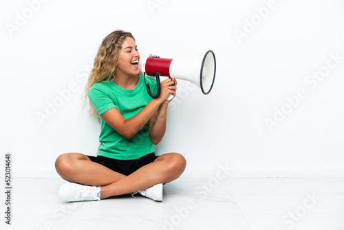 Girl with curly hair sitting on the floor shouting through a megaphone