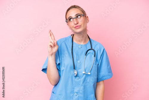Young surgeon nurse woman isolated on pink background with fingers crossing and wishing the best